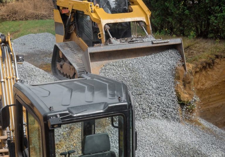 Construction machinery spreading gravel for road construction with trees in the background on a cloudy day.